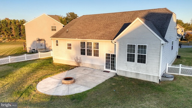 rear view of property with an outdoor fire pit, a shingled roof, fence, a yard, and a patio area