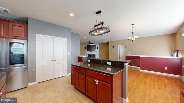 kitchen with a fireplace, a kitchen island, visible vents, refrigerator with glass door, and decorative light fixtures