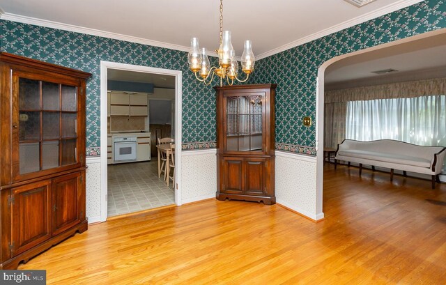 unfurnished dining area featuring an inviting chandelier, crown molding, and light hardwood / wood-style flooring