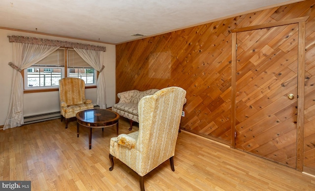 sitting room featuring a baseboard radiator, ornamental molding, wood-type flooring, and wooden walls