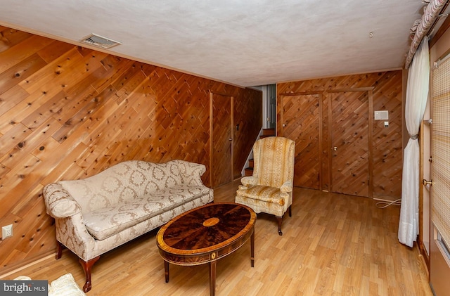 sitting room featuring light wood-type flooring, a textured ceiling, wooden walls, and a barn door