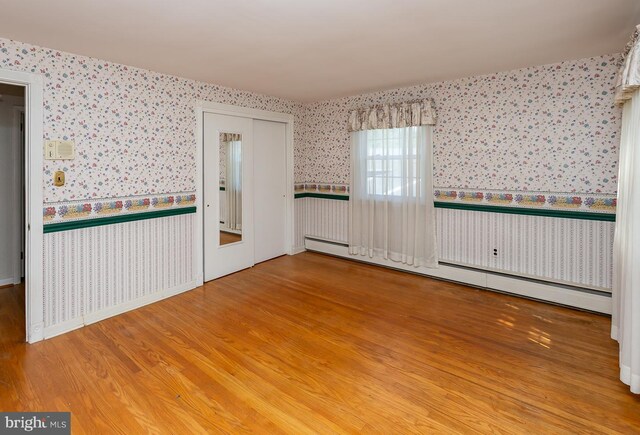 unfurnished room with a baseboard heating unit and hardwood / wood-style floors