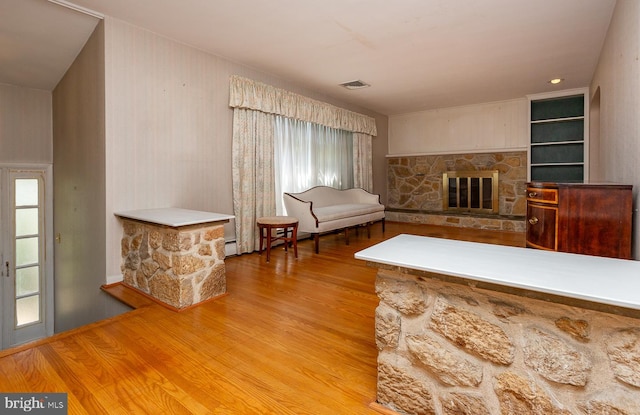 unfurnished living room with hardwood / wood-style floors, a baseboard radiator, wooden walls, and a stone fireplace