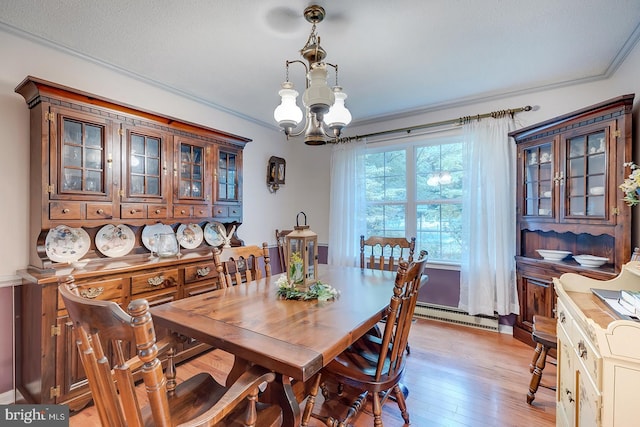 dining room featuring light wood-type flooring, a textured ceiling, a notable chandelier, baseboard heating, and ornamental molding