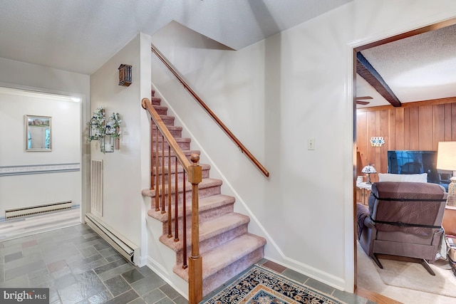 staircase featuring a textured ceiling, wooden walls, baseboard heating, and beamed ceiling