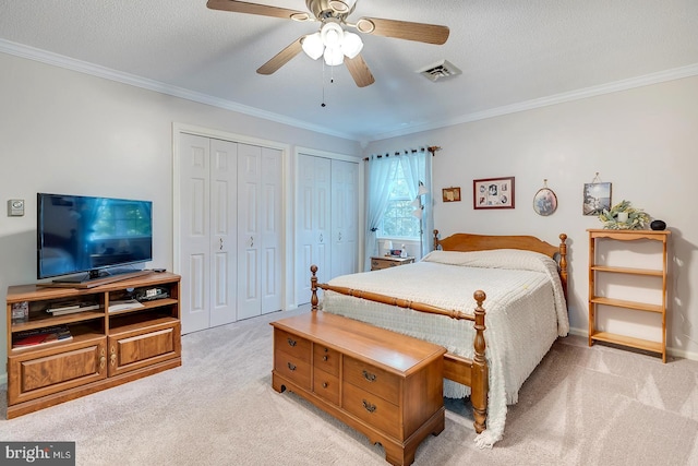 bedroom with ceiling fan, ornamental molding, a textured ceiling, two closets, and light carpet