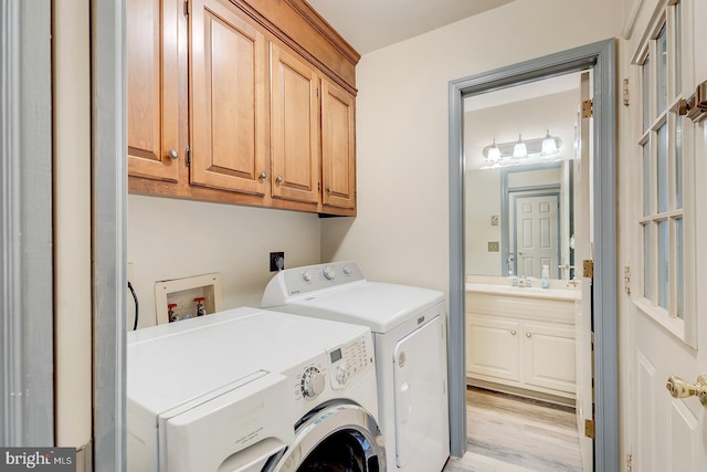 laundry room with light wood-type flooring, separate washer and dryer, and cabinets