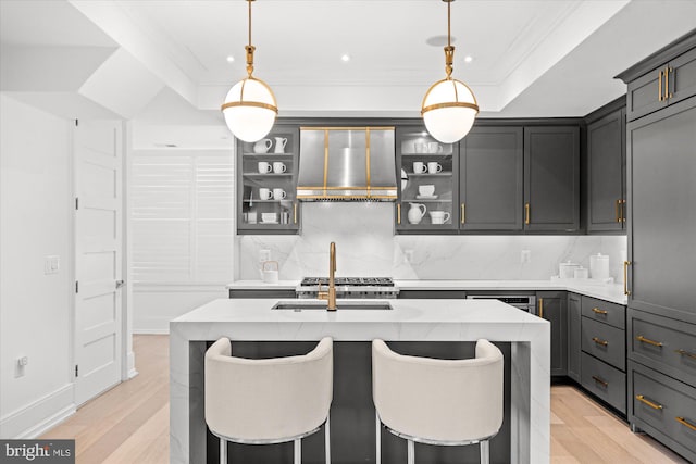 kitchen with light hardwood / wood-style floors, tasteful backsplash, wall chimney exhaust hood, a breakfast bar area, and a kitchen island with sink