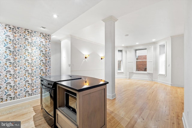 kitchen featuring a kitchen island, ornate columns, light wood-type flooring, crown molding, and electric range