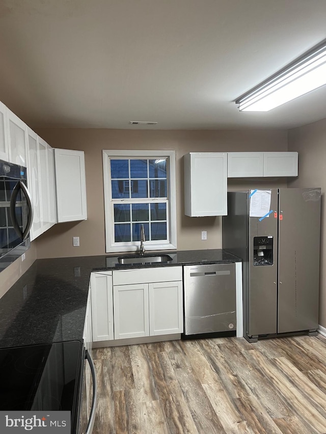 kitchen with dark stone countertops, sink, white cabinetry, appliances with stainless steel finishes, and light hardwood / wood-style floors