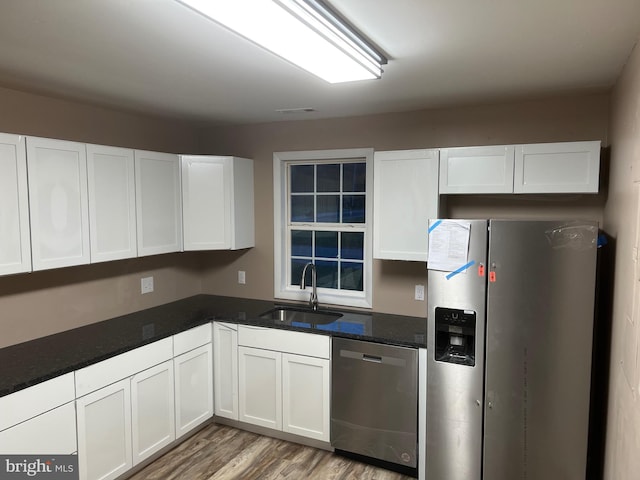 kitchen featuring sink, white cabinetry, light hardwood / wood-style floors, stainless steel appliances, and dark stone counters