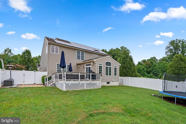 back of property featuring a wooden deck, a yard, a trampoline, and central AC