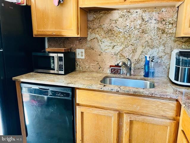 kitchen featuring light stone countertops, black dishwasher, sink, and decorative backsplash