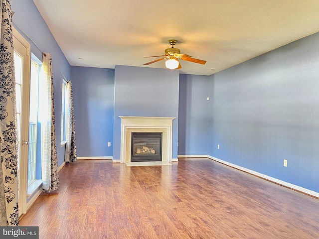 unfurnished living room featuring ceiling fan, baseboards, a fireplace with flush hearth, and wood finished floors