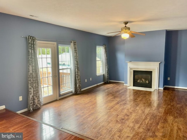 unfurnished living room featuring a ceiling fan, wood finished floors, visible vents, baseboards, and a fireplace with flush hearth