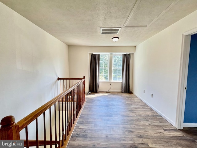 hallway with visible vents, an upstairs landing, a textured ceiling, wood finished floors, and baseboards