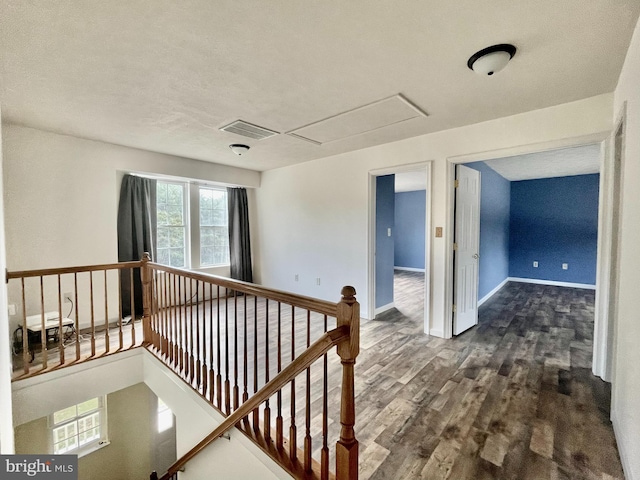 corridor featuring visible vents, baseboards, attic access, dark wood-style flooring, and an upstairs landing