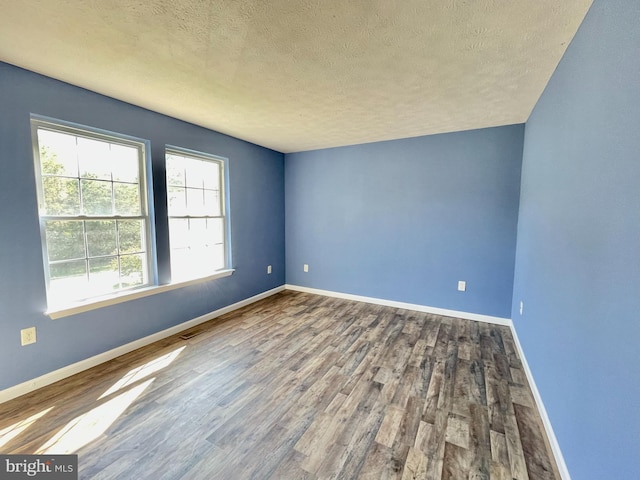 empty room featuring visible vents, baseboards, a textured ceiling, and wood finished floors