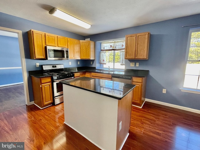 kitchen with a sink, dark countertops, dark wood-style floors, appliances with stainless steel finishes, and baseboards