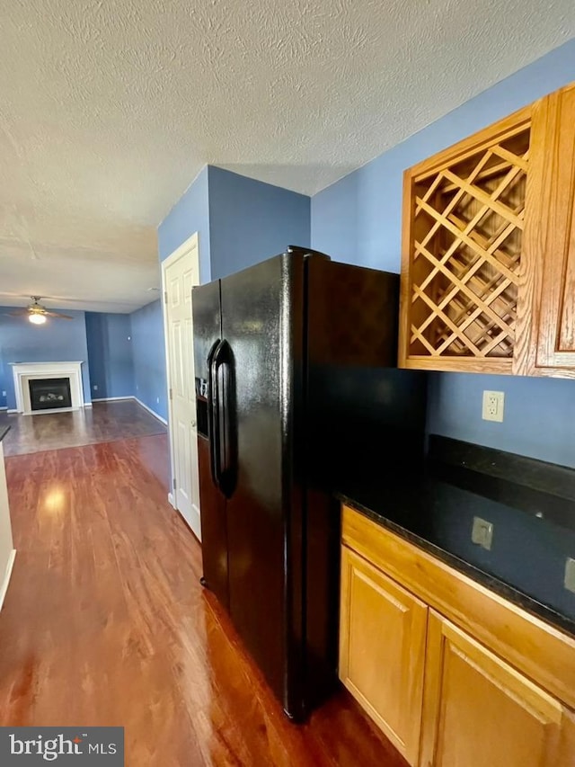 kitchen with dark wood-style floors, a fireplace, ceiling fan, a textured ceiling, and black fridge