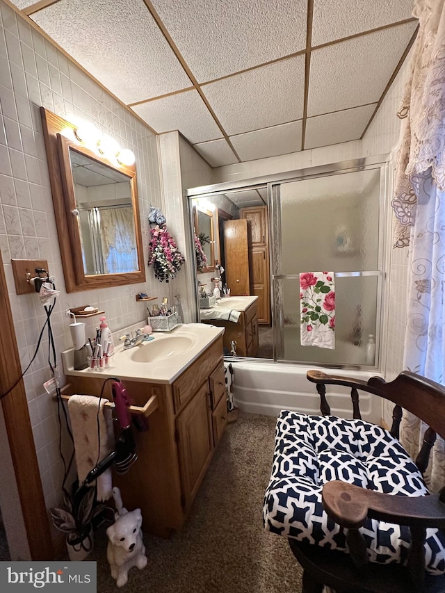 bathroom with a drop ceiling, vanity, tile walls, and enclosed tub / shower combo