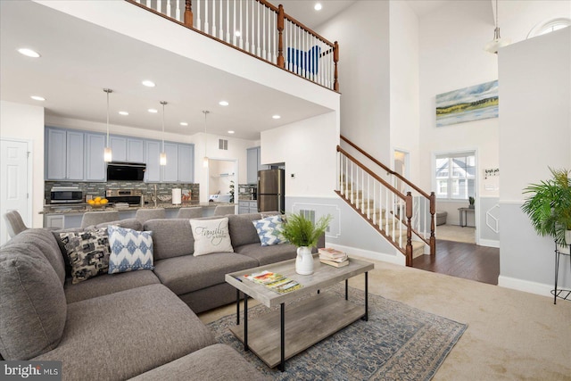 living area featuring a towering ceiling, stairs, dark colored carpet, and recessed lighting