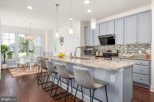 kitchen with dark hardwood / wood-style flooring, stainless steel electric stove, decorative light fixtures, and a center island with sink