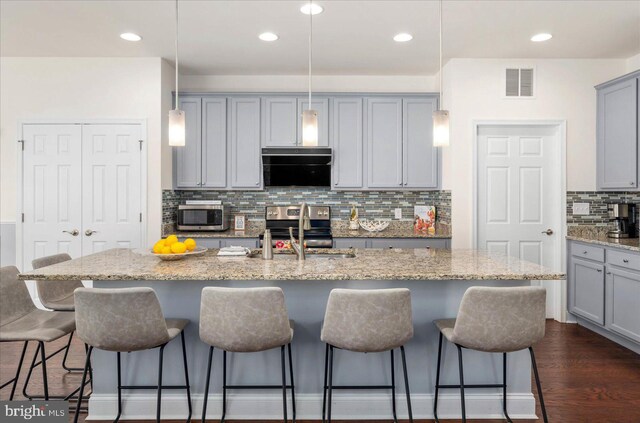 kitchen featuring a center island with sink, light stone counters, and a kitchen bar