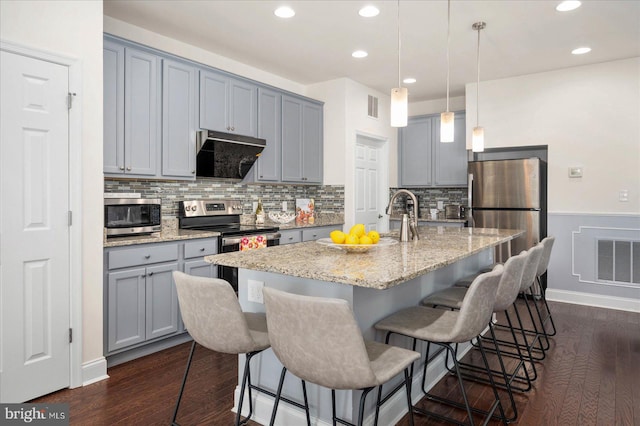 kitchen featuring dark wood-type flooring, a breakfast bar area, a center island with sink, and extractor fan