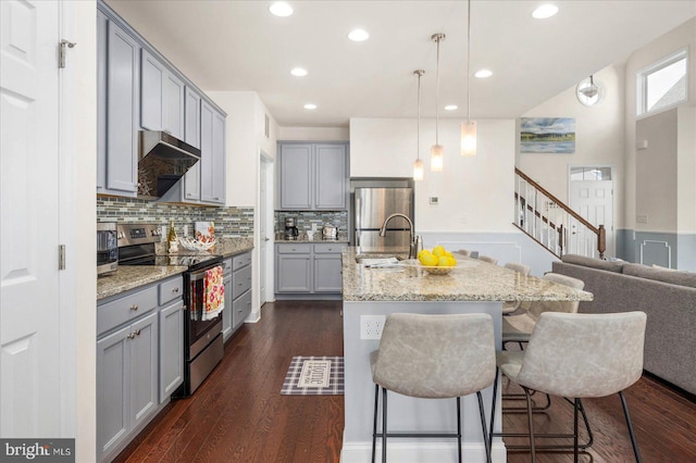 kitchen featuring hanging light fixtures, a kitchen bar, dark wood-type flooring, light stone countertops, and appliances with stainless steel finishes