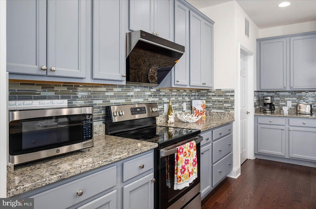 kitchen with gray cabinets, tasteful backsplash, light stone countertops, dark wood-type flooring, and appliances with stainless steel finishes