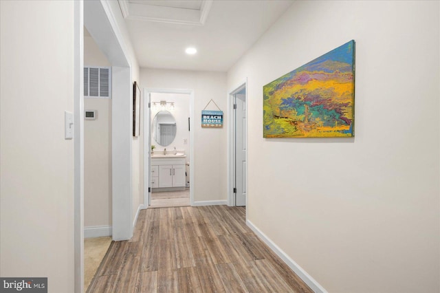 hallway featuring a sink, attic access, baseboards, and wood finished floors