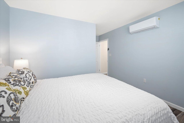 bedroom with a wall unit AC, baseboards, and wood finished floors