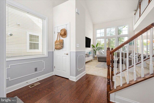 entrance foyer with high vaulted ceiling, visible vents, stairway, wainscoting, and dark wood finished floors