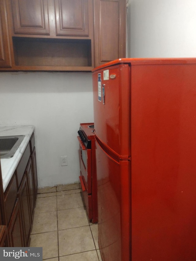 kitchen featuring fridge, sink, black stove, and light tile patterned floors