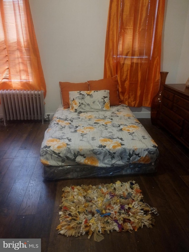 bedroom with radiator heating unit and dark hardwood / wood-style flooring