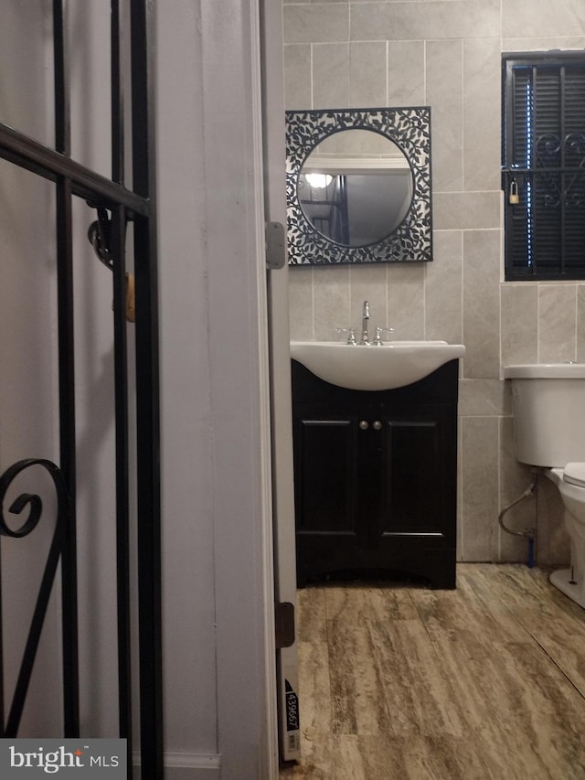 bathroom with tile walls, hardwood / wood-style flooring, vanity, and toilet