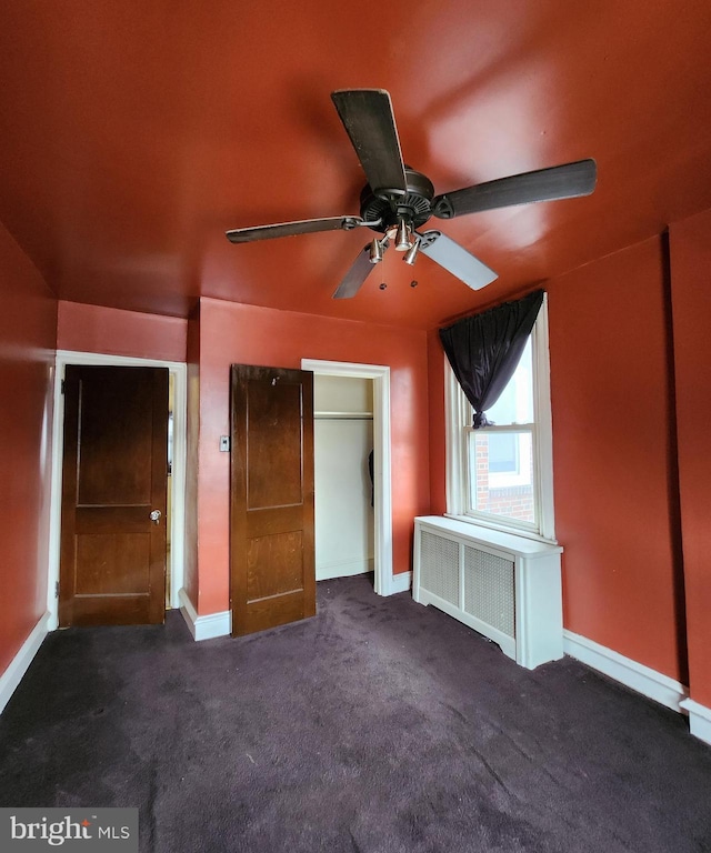 unfurnished bedroom featuring radiator, ceiling fan, and dark carpet