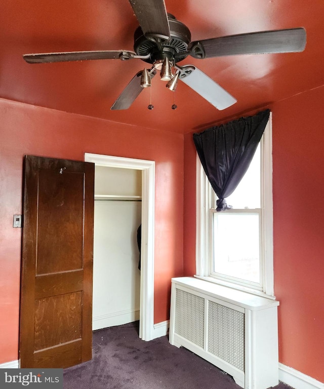 unfurnished bedroom featuring ceiling fan, a closet, dark colored carpet, and radiator heating unit