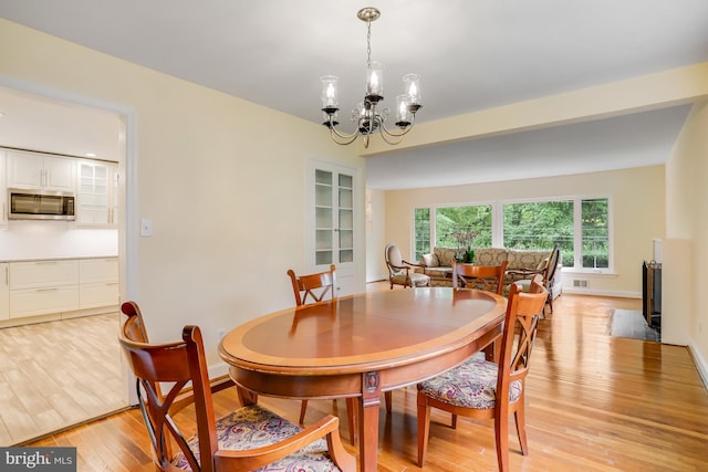dining room featuring light wood finished floors, visible vents, baseboards, and an inviting chandelier