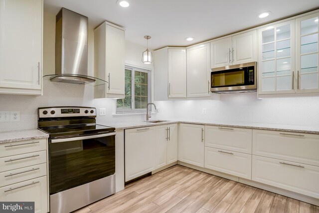 kitchen with light hardwood / wood-style floors, wall chimney exhaust hood, hanging light fixtures, white cabinetry, and appliances with stainless steel finishes