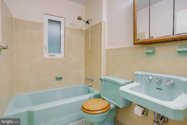 bathroom with a sink, tile walls, toilet, wainscoting, and shower / tub combination