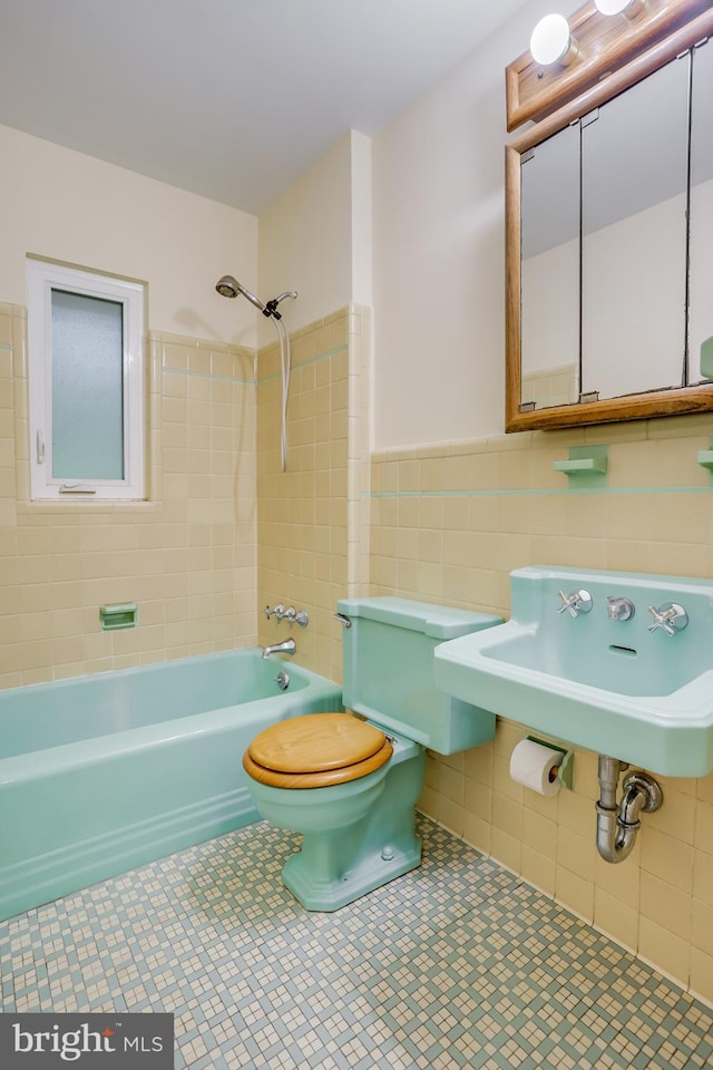 bathroom featuring toilet, wainscoting, tile walls, tile patterned floors, and shower / bathing tub combination