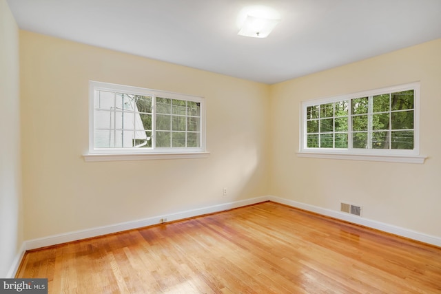empty room with wood finished floors, baseboards, and visible vents