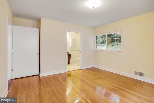 unfurnished bedroom with visible vents, light wood-type flooring, baseboards, and ensuite bathroom