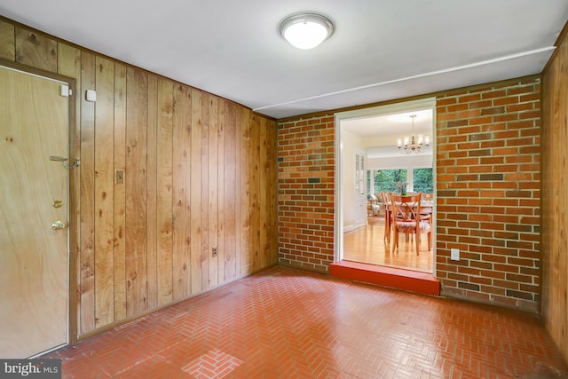 unfurnished room with wood walls, a notable chandelier, and brick floor
