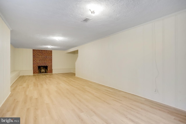 basement featuring a brick fireplace, light hardwood / wood-style floors, ornamental molding, and a textured ceiling