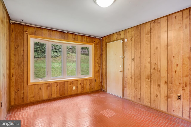 spare room with wooden walls, baseboards, and brick floor