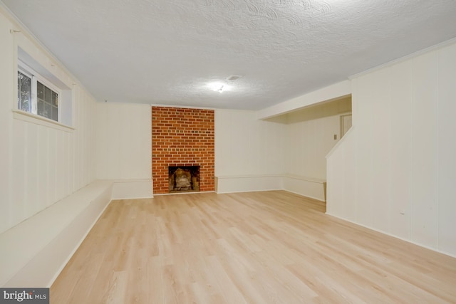 basement featuring a brick fireplace, a textured ceiling, and light hardwood / wood-style flooring