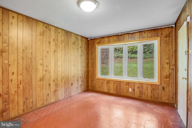 unfurnished room featuring wood walls, brick floor, and baseboards